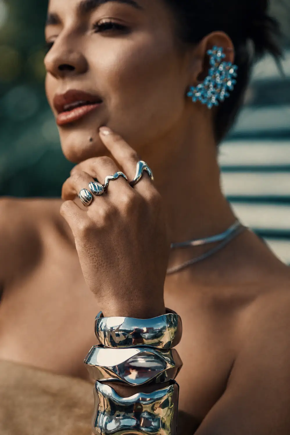Modelo de perfil com brinco statement de pedras azuis, anéis esculturais e braceletes de prata da coleção Allure